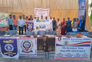 Group of men and women posing behind a long table with banners at an outdoor event.