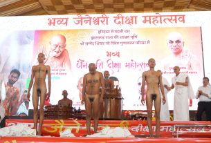 Three unclothed men standing on a stage during a Hindu religious event, with a large banner and portraits in the background.