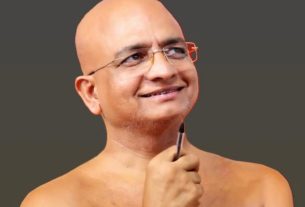 Smiling bald man with glasses, holding a pen to his chin as he looks upward.