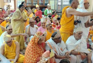 Group of people in traditional Indian attire, many wearing turbans, gathered for a religious ceremony in a community hall/temple setting.
