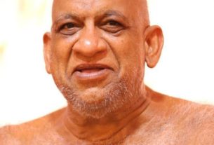 Close-up of a smiling bald man with gray stubble, shoulders visible.