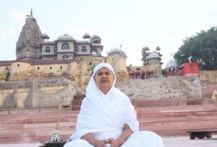 Woman in white headscarf sits on red stone steps in front of a historic temple complex with old architecture in the background.