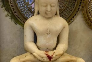 Stone Buddha statue in a seated meditation pose with a decorative circular halo behind him.