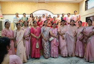 Group of women in pink sarees posing for a group photo at a community event indoors.