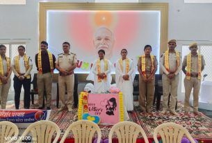 Group of uniformed men and women wearing yellow sashes stand in a line on a stage with a large portrait backdrop and a Mother's Day banner in front.