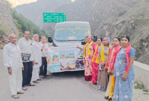 Group of Indian men and women posing with a banner in front of a tour bus on a mountain highway road edge area of a gorge valley.