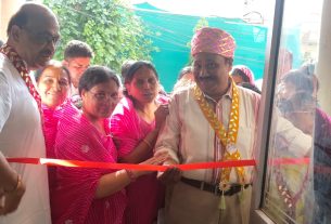 A ribbon-cutting ceremony with several people in pink outfits gathered around a red ribbon at a doorway.