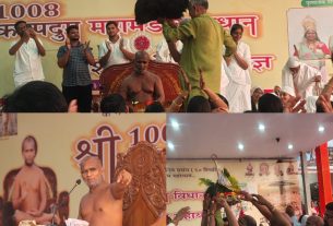 Crowd at a Hindu temple rally with a seated guru on ornate chair and performers clapping in front of a yellow banner in Hindi.
