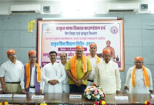 Group of men in white and saffron outfits posing in front of a Hindi banner at a formal event.