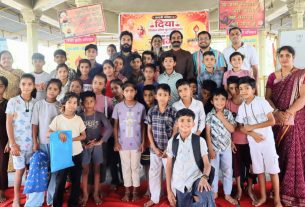 Group of children and adults posing for a group photo at a community event with Hindi banners in the background.
