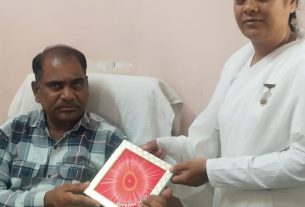 Nurse in a white uniform hands a red card to a seated man in a clinic.
