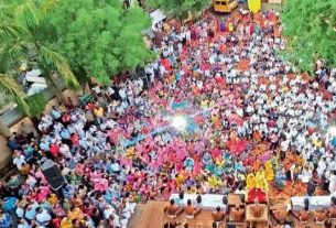 Aerial view of a large outdoor crowd in a green courtyard surrounding a central stage for a ceremony or event.